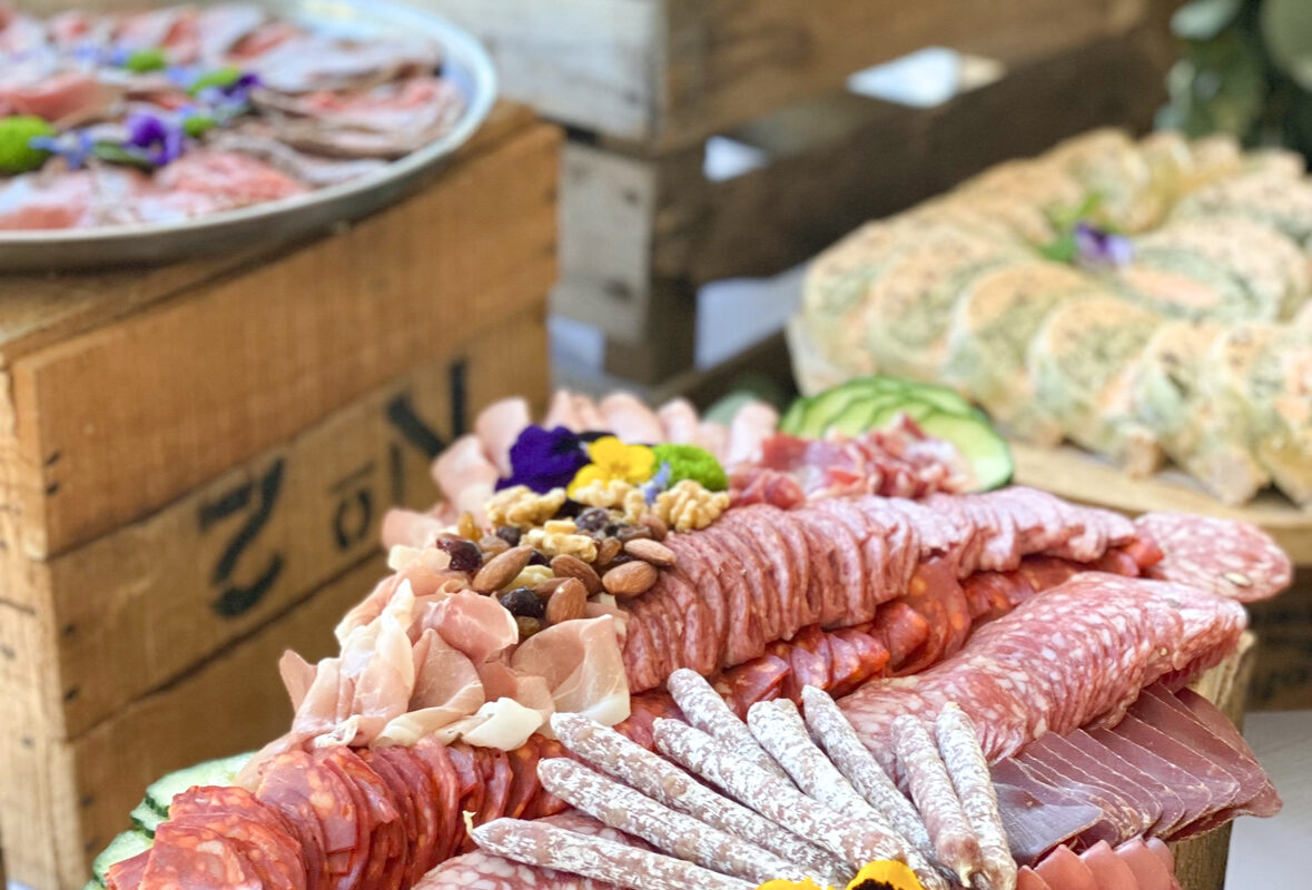 Planche de charcuterie, roulés de saumon et plateaux de pièces cocktail dressés sur des caisses en bois par Saisons Traiteur