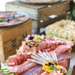 Planche de charcuterie, roulés de saumon et plateaux de pièces cocktail dressés sur des caisses en bois par Saisons Traiteur